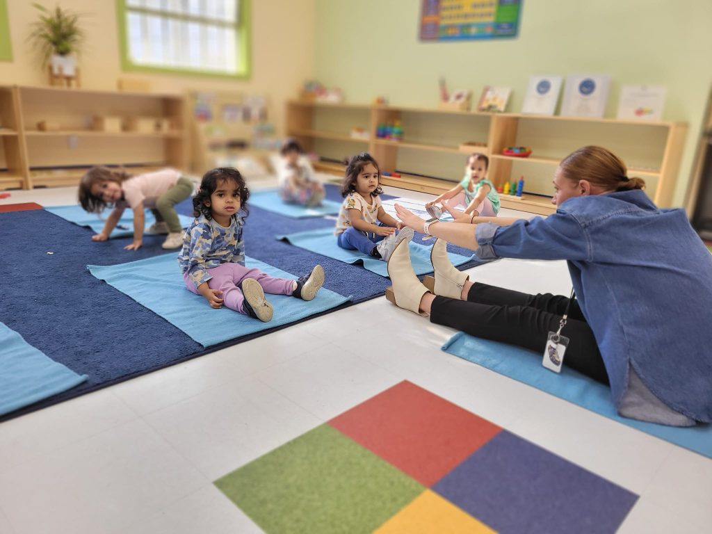 Daycare in Irvington (Fremont) California; a teach touching her toes and the toddlers looking on with attention.