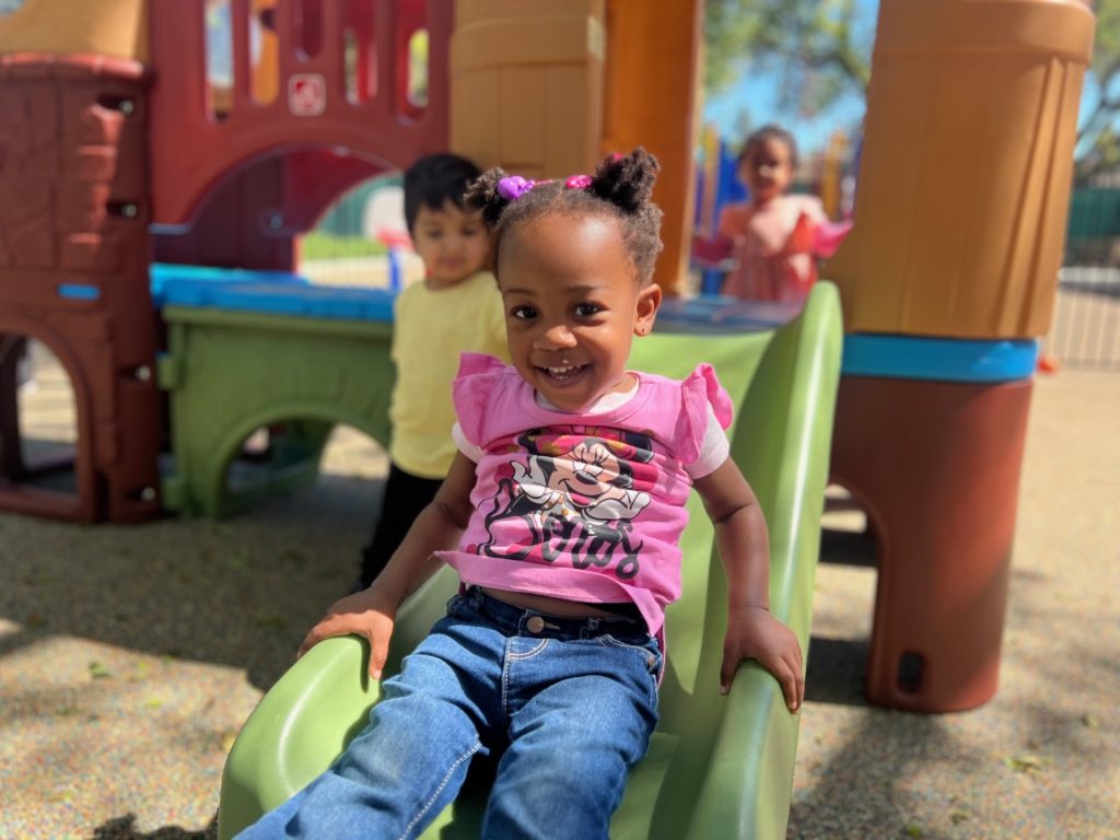 Happy young girl, exploring outdoor fun at a preschool in Fremont, California.
